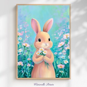 Puede incluir: Una impresión artística enmarcada que presenta un conejito sosteniendo un ramo de flores blancas. El conejito es de color melocotón suave con orejas rosas, sobre un fondo de follaje azul y verde y flores silvestres. La impresión está firmada "Wisterelle Prints" en la parte inferior.