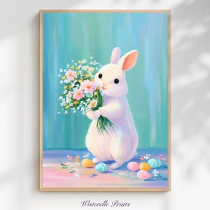 Puede incluir: Una impresión enmarcada que presenta un conejito blanco sosteniendo un ramo de flores rosas y blancas. Huevos de Pascua de colores pastel están esparcidos en el suelo. El fondo es de color turquesa y azul suave. El texto "Wisterelle Prints" está abajo.