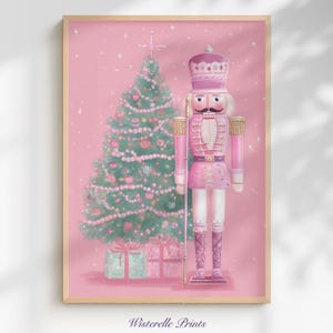 Può includere: Una stampa incorniciata con un tema natalizio rosa. L'opera raffigura un soldato schiaccianoci rosa con una corona, un albero di Natale decorato e regali confezionati. Lo sfondo è rosa tenue con neve che cade. Il testo "Wisterelle Prints" è in basso.