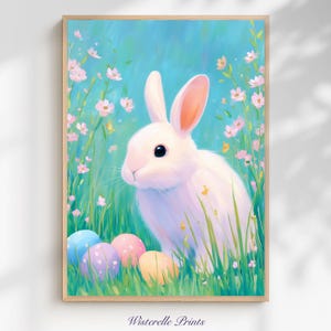 Puede incluir: Una impresión enmarcada que presenta un conejo blanco con orejas rosadas, rodeado de hierba verde, flores rosas y coloridos huevos de Pascua. El fondo es azul claro. La impresión está etiquetada como "Wisterelle Prints".