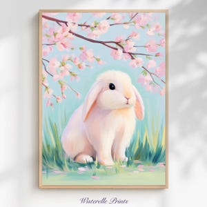 Puede incluir: Una impresión artística enmarcada que presenta un conejo blanco con orejas largas, sobre un fondo de flores de cerezo rosas y un cielo azul claro. El conejo está en hierba verde, con el texto "Wisterelle Prints" en la parte inferior.