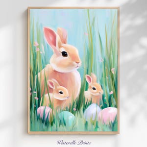 Puede incluir: Una impresión enmarcada que presenta una familia de conejos en medio de hierba alta y verde y huevos de Pascua de colores pastel. Los conejos tienen pelaje color melocotón y orejas rosas. El fondo es azul suave con pétalos de flores rosas. El texto "Wisterelle Prints" está en la parte inferior.