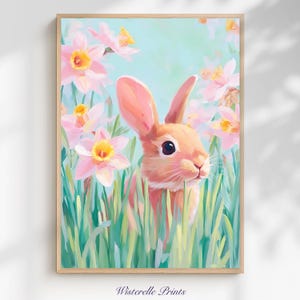Puede incluir: Una impresión artística enmarcada que presenta un conejo color melocotón entre narcisos rosas y amarillos y hierba verde. El conejo tiene orejas grandes y ojos oscuros. El fondo es de un suave azul verdoso. La impresión está firmada "Wisterelle Prints".