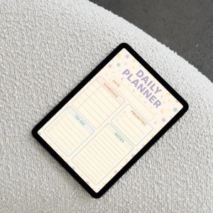 May include: A black tablet displaying a "Daily Planner" layout. The planner features sections for scheduling, to-do lists, priorities, and notes, with pastel color blocks and star and moon graphics.