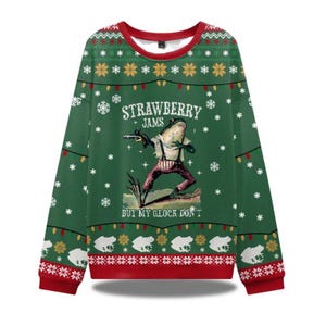 May include: Green Christmas sweater with a red collar and cuffs. The sweater features a frog graphic with the text "STRAWBERRY JAMS BUT MY GLOCK DON'T". The design includes snowflakes, string lights, and frog silhouettes.