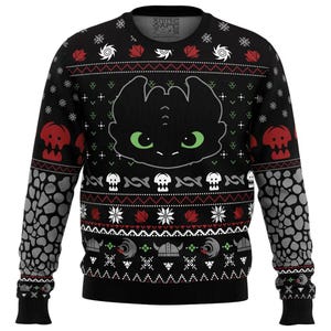 May include: Black crew neck sweater featuring a cartoon dragon face with green eyes. The sweater has a repeating pattern of skulls, snowflakes, and Viking helmets in red, white, and gray. The sleeves have a gray stone pattern.