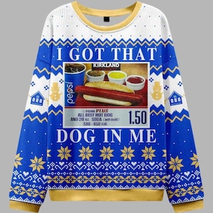 Puede incluir: Un suéter blanco, azul y amarillo con un gráfico de un perrito caliente y refresco, y el texto "I GOT THAT DOG IN ME". El suéter tiene cuello y puños acanalados, y un patrón festivo.