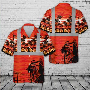 Op de afbeelding: Oranje shirt met korte mouwen met een tropisch zonsondergangontwerp met palmbomen en bloemen. Het shirt heeft reflecterende zilveren strepen en een afbeelding van figuren op de onderkant van de voor- en achterkant.