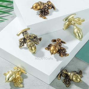 Op de afbeelding: Verschillende eikelvormige kastknoppen in verschillende tinten goud en brons. Elke knop heeft een eikelontwerp met gedetailleerde bladeren, perfect om een vleugje door de natuur geïnspireerde elegantie aan meubels toe te voegen.