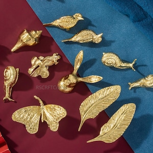 Op de afbeelding: Een set van drie keramische mokken met een gespikkelde, matte afwerking. De mokken zijn in de kleuren crème, lichtgrijs en donkergrijs. Elke mok heeft een eenvoudig, minimalistisch ontwerp en een afgeronde handgreep.