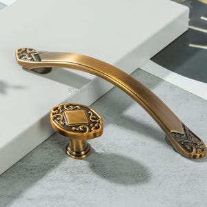 以下が含まれることがあります： アンティーク真鍮のキャビネット金具セット。カーブしたハンドルと装飾的なノブが含まれています。金具は、装飾的なディテールと暖かく、古びた仕上げが特徴で、家具にヴィンテージ感を加えるのに最適です。