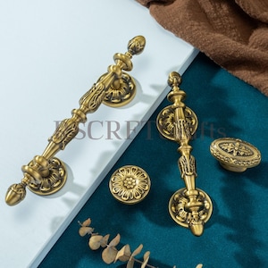 May include: Ornate antique brass door handles and knobs. The handles have a detailed floral and scroll design. The knobs include a round floral design and an oval design with a starburst pattern. The text "SECRET gifts" is visible on the handles.