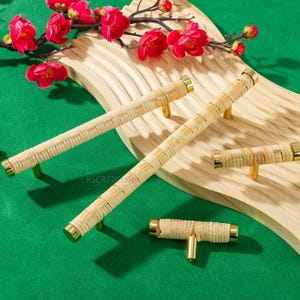 May include: Four woven rattan cabinet pulls and knobs with brass accents. The hardware is displayed on a light wood surface with a green background and red flowers.