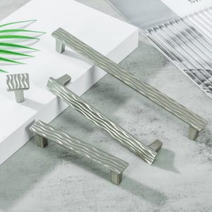 以下が含まれることがあります： シルバーカラーのキャビネットハードウェアのコレクション。3つの異なるサイズのプルと正方形のノブが含まれています。ハードウェアは、テクスチャ加工された波状のデザインが特徴です。アイテムは白い表面と灰色の背景に配置されています。