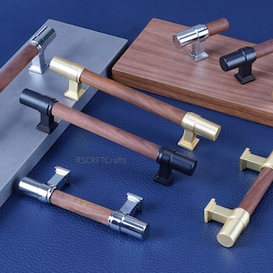 May include: A collection of cabinet hardware, including handles and knobs. The handles feature a dark wood grain center with silver, gold, and black metal accents. The knobs have a similar design. The hardware is displayed on gray and brown surfaces against a blue background.