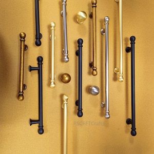 Peut inclure: Une sélection de poignées de porte et de boutons en différentes finitions métalliques, dont le noir, l'or et l'argent. Les poignées sont de longueurs et de designs variés, avec des styles de barres et de boutons. Le fond est de couleur or chaud.