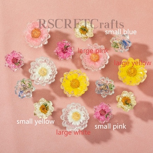 May include: A collection of pressed flowers encased in clear resin, featuring various colors including pink, yellow, white, and blue. The image includes text labels such as RSCFTCrafts, small blue, large pink, large yellow, small yellow, and small pink.