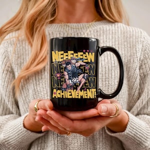 以下が含まれることがあります： 黒いセラミックマグカップ。格闘ポーズの2人の人物、黄色の「NEEEFEW ACHIEVEMENT！」の文字、トロフィーが描かれたラップアラウンドグラフィック。マグカップには黒いハンドルが付いています。