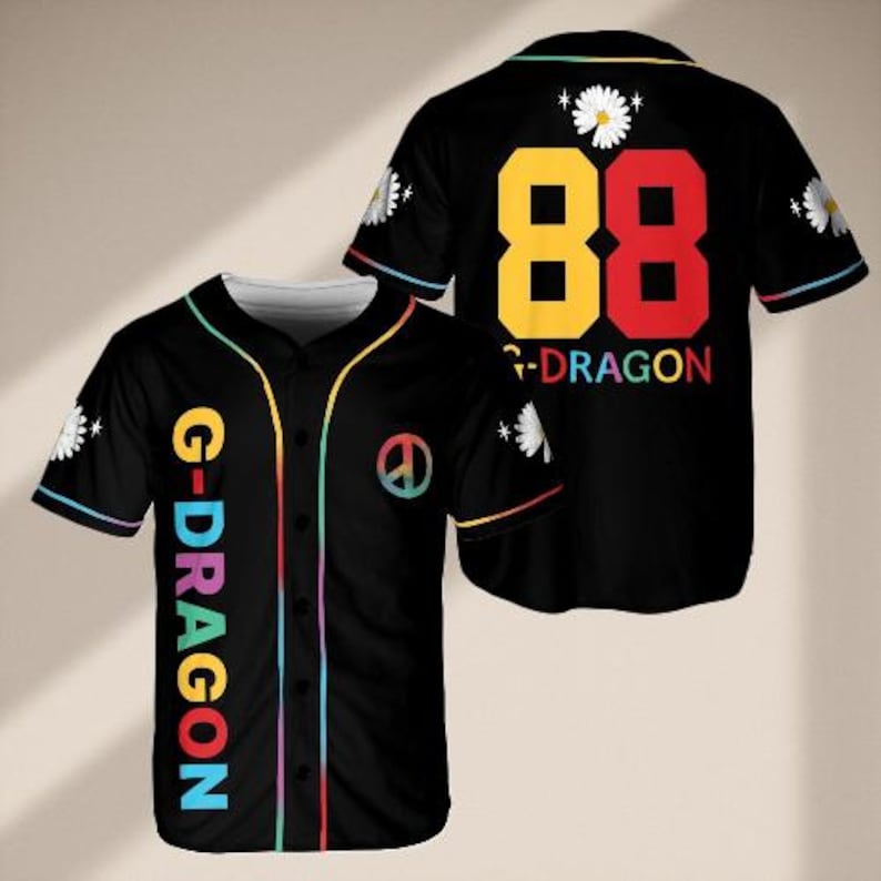 May include: Black baseball jersey with colourful accents. Features the text "G-DRAGON" vertically on the front and "88" with "G-DRAGON" on the back. Includes a peace symbol and daisy graphics. The jersey has a button-up front and short sleeves.