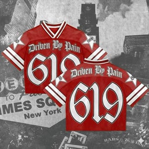 May include: Red mesh jersey with white accents, featuring the text "Driven By Pain" and the number "619" in a bold, stylized font. The jersey has a V-neck collar and white stripes on the sleeves. The background is a grayscale image of a city.