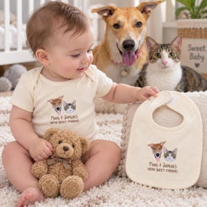 Puede incluir: Un body para bebé y un babero a juego de color crema, ambos con retratos bordados de un perro y un gato con el texto "Fran & James's NEW BEST FRIEND" en hilo marrón. El conjunto se muestra junto a un oso de peluche de color marrón.