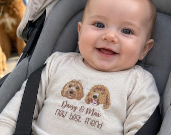 May include: A long-sleeved beige baby bodysuit featuring an embroidered design of two brown curly-haired dogs. Below the dogs, the text reads Daisy & Max new best friend in brown lettering. The garment has a crew neckline and ribbed cuffs.
