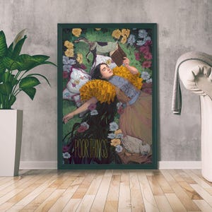 May include: A framed art print featuring a woman lying in a field of flowers, reading a book. The artwork has a vintage aesthetic with the words "POOR THINGS" at the bottom. The color palette includes greens, yellows, and browns.