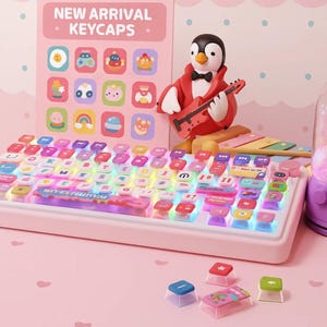 May include: A pink mechanical keyboard with colorful, illuminated keycaps. The keyboard has a matching pink base and features a penguin figurine playing a guitar. The background includes a display of keycap designs and the text "NEW ARRIVAL KEYCAPS."