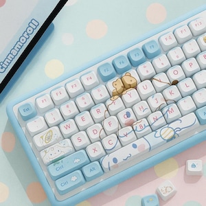 May include: A light blue mechanical keyboard with white keycaps featuring cartoon character designs. The keyboard has a matching light blue frame and includes additional keycaps. The word "Cinnamoroll" is printed on the side.