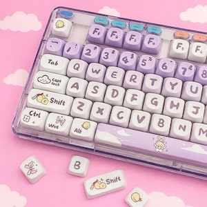 May include: A clear, rectangular keyboard with white and lavender keycaps. The keys are arranged in a standard QWERTY layout. Some keys have decorative illustrations of clouds, butterflies, and fruit. The keyboard has a clear plastic frame.