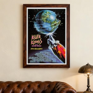Op de afbeelding: Een ingelijste filmposter voor "Killer Klowns from Outer Space". De poster toont een kleurrijke illustratie van een clownshand die een planeet Aarde op zijn vinger balanceert. De titeltekst is rood en de slogan luidt "It's Craazzy!"