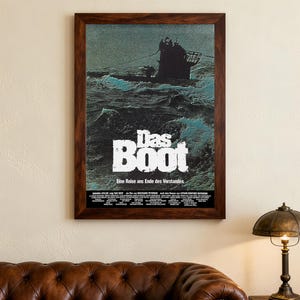 May include: A framed movie poster for "Das Boot" showing a dark submarine on turbulent waters. The title, in bold white letters, is above German text. The poster is in a dark wooden frame, suitable for a home cinema.