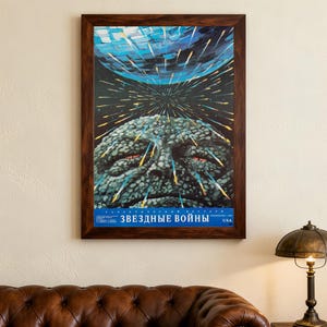 Op de afbeelding: Ingelijste vintage poster met een ruimte-thema illustratie. Het kunstwerk toont een groot, getextureerd gezicht met rode ogen, een blauwe planeet en lichtstrepen. De poster zit in een donkere houten lijst.