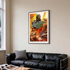 May include: A framed poster for Star Wars: The Mandalorian and Grogu. The artwork depicts the Mandalorian, Grogu, and other characters in a dynamic scene with a fiery background. The poster is displayed above a black leather sofa in a living room setting.