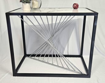 Mesa consola de acero con tablero de baldosas con apariencia de mármol y detalle de aguja en tono plateado radiante.