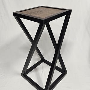 May include: A modern side table with a geometric design. The table features a dark brown wooden top set within a black metal frame. The frame has an X-shaped design on the sides, creating a visually interesting and stable base.