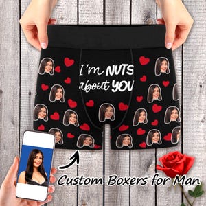 May include: Black boxer shorts with a repeating pattern of red hearts and a woman's face. The text "I'm NUTS about YOU" is printed on the front. A smartphone displays the same woman's face. A red rose is in the image.