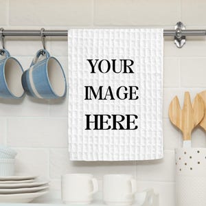 May include: White waffle-weave kitchen towel with the text "YOUR IMAGE HERE" in black. The towel hangs from a silver bar, with blue mugs and white dishes in the background. Wooden utensils are in a white container.