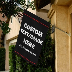 May include: A black flag with the text "CUSTOM TEXT/IMAGE HERE" in white, with a red border and stars. The flag is mounted on a silver pole and displayed outside a building.