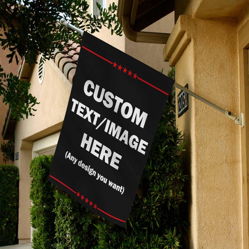 May include: A black flag with the text "CUSTOM TEXT/IMAGE HERE" in white, with a red border and stars. The flag is mounted on a silver pole and displayed outside a building.