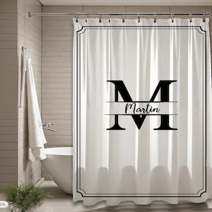May include: White shower curtain with a black border and a large black letter "M" with the name "Martin" underneath. The curtain is hanging in a bathroom with a white bathtub and a towel.