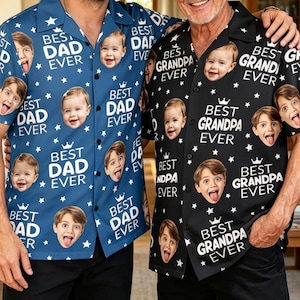 May include: Two short-sleeved button-down shirts featuring a repeating pattern of small white stars, crowns, and faces of children. The blue shirt displays the text BEST DAD EVER, while the black shirt displays the text BEST GRANDPA EVER.