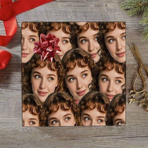 May include: Square gift wrap featuring a repeating pattern of a woman's face with brown hair and a red bow. The background is a wooden surface with red ribbon and gold scissors.