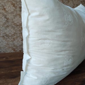 May include: A white pillow with a repeating circular pattern. The pillow is on a wooden surface. The pillow has a folded edge. The pattern includes the words "PREMIUM QUALITY".