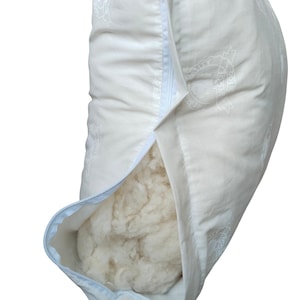 Puede incluir: Una almohada blanca parcialmente desabrochada, revelando el relleno suave y claro. La funda de almohada tiene un patrón sutil y una cremallera azul claro. La imagen sugiere comodidad y calidad, ideal para el dormitorio.
