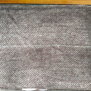 May include: A folded brown and white herringbone patterned blanket. The blanket has a soft, textured appearance with a repeating diagonal stripe design. The color is a muted brown with white accents.