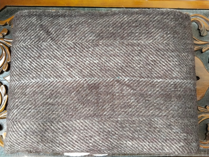 May include: A folded brown and white herringbone patterned blanket. The blanket has a soft, textured appearance with a repeating diagonal stripe design. The color is a muted brown with white accents.
