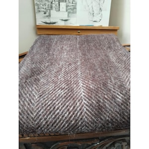 May include: A brown and white herringbone patterned fabric, likely wool or a wool blend, covers a seat. The fabric's pattern creates a visual texture. The seat is part of a wooden chair with carved details.