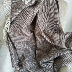 May include: A brown and white herringbone pattern throw blanket draped over a chair. The blanket has a fringed edge and is made of a soft, woven material. The color palette is neutral, with shades of brown and white.