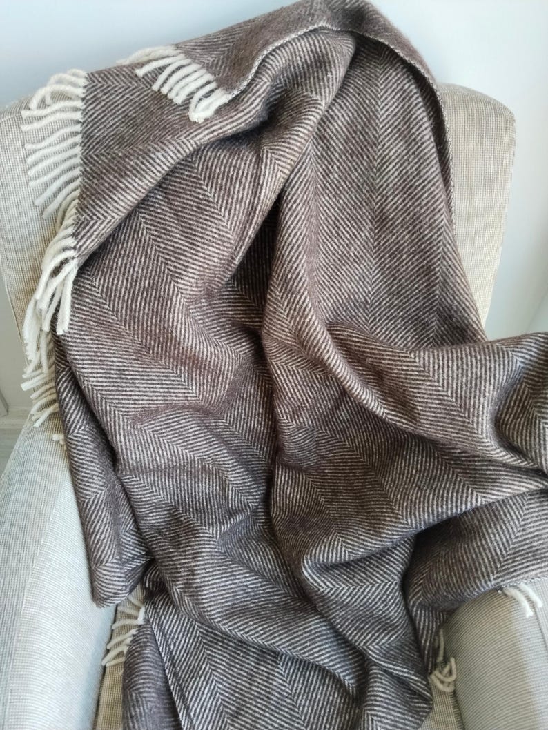May include: A brown and white herringbone pattern throw blanket draped over a chair. The blanket has a fringed edge and is made of a soft, woven material. The color palette is neutral, with shades of brown and white.